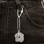 Close-up of a silver keychain with a tag attached to a black denim trouser.