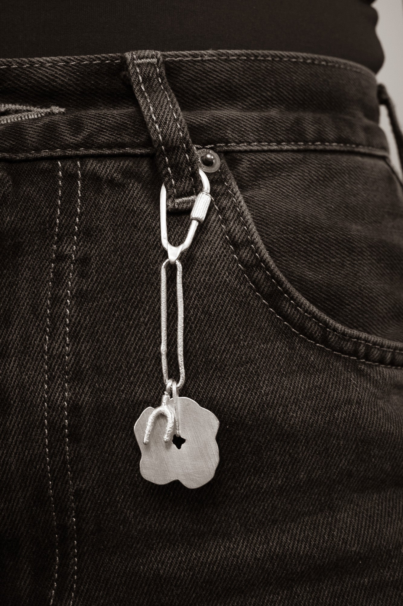 Close-up of a silver keychain with a tag attached to a black denim trouser.