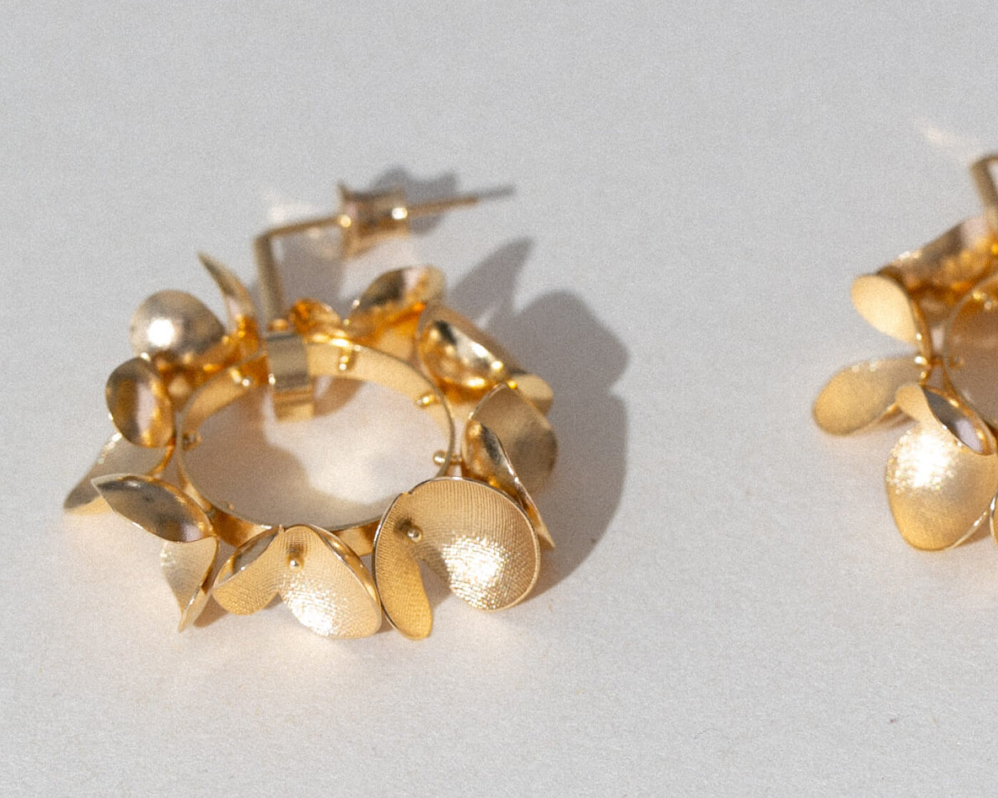 Gold hoop earrings with leaf-like designs on a light gray background