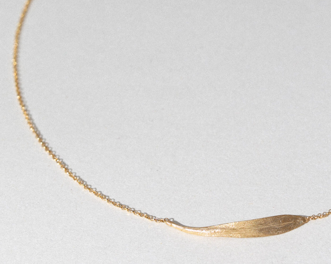 Gold necklace with a leaf-shaped pendant on a light gray background