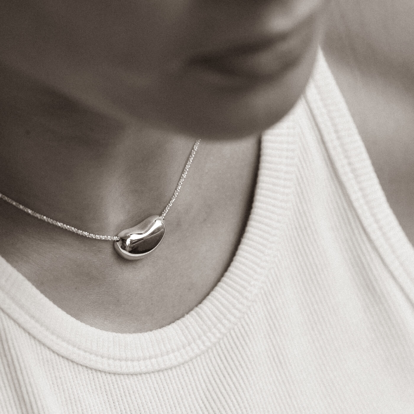 Silver necklace with a heart-shaped pendant worn by a person in a white top.