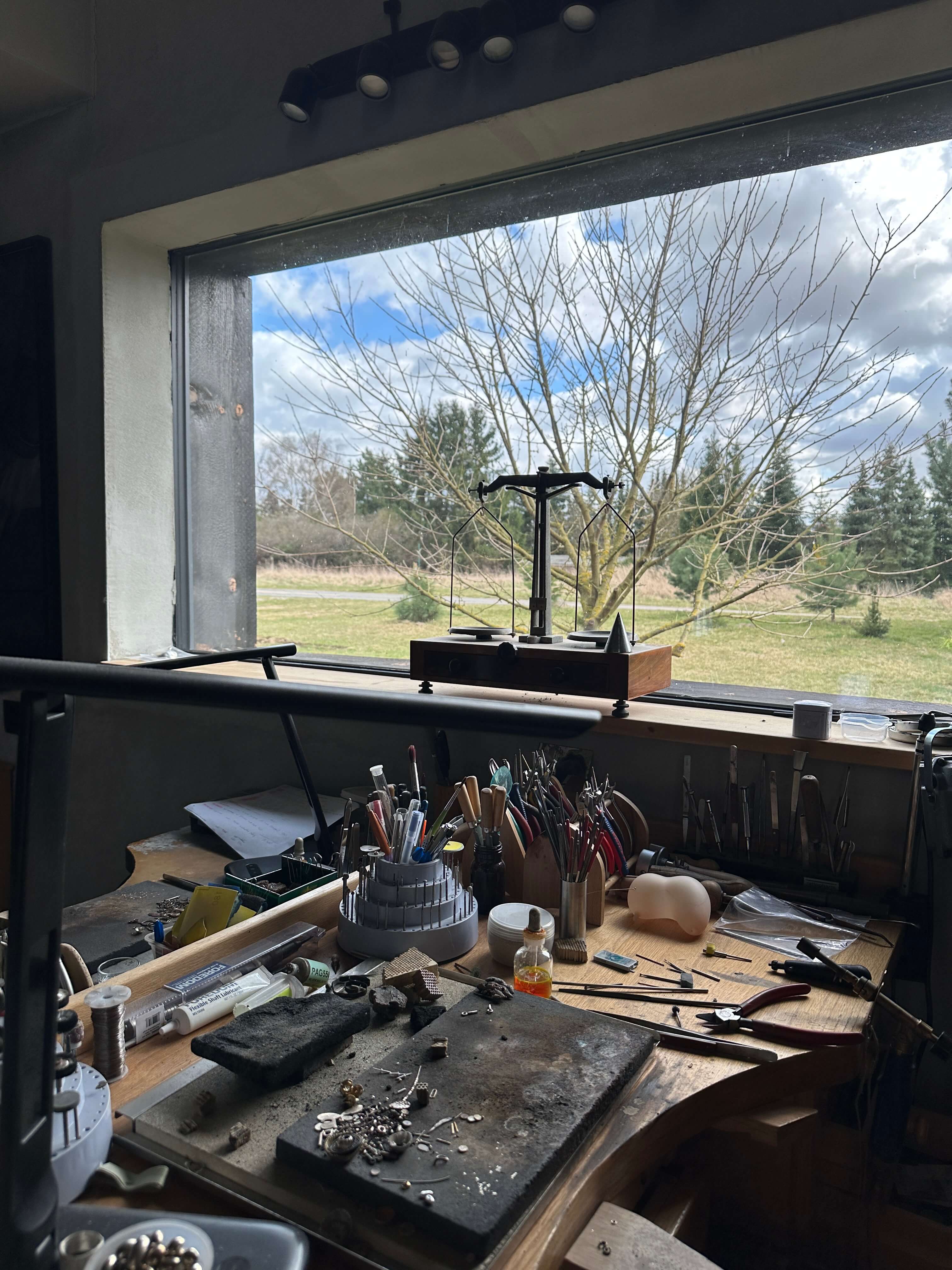 Workbench with tools and materials in a room with large windows showing a view of trees and sky.