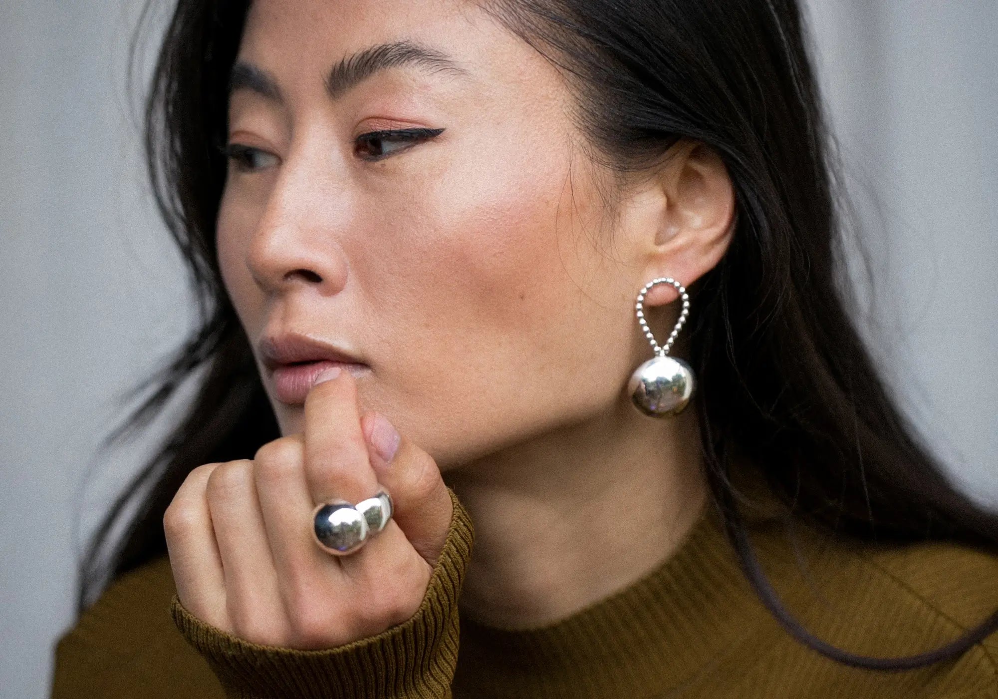 Woman wearing silver hoop earrings and ring, with a neutral background