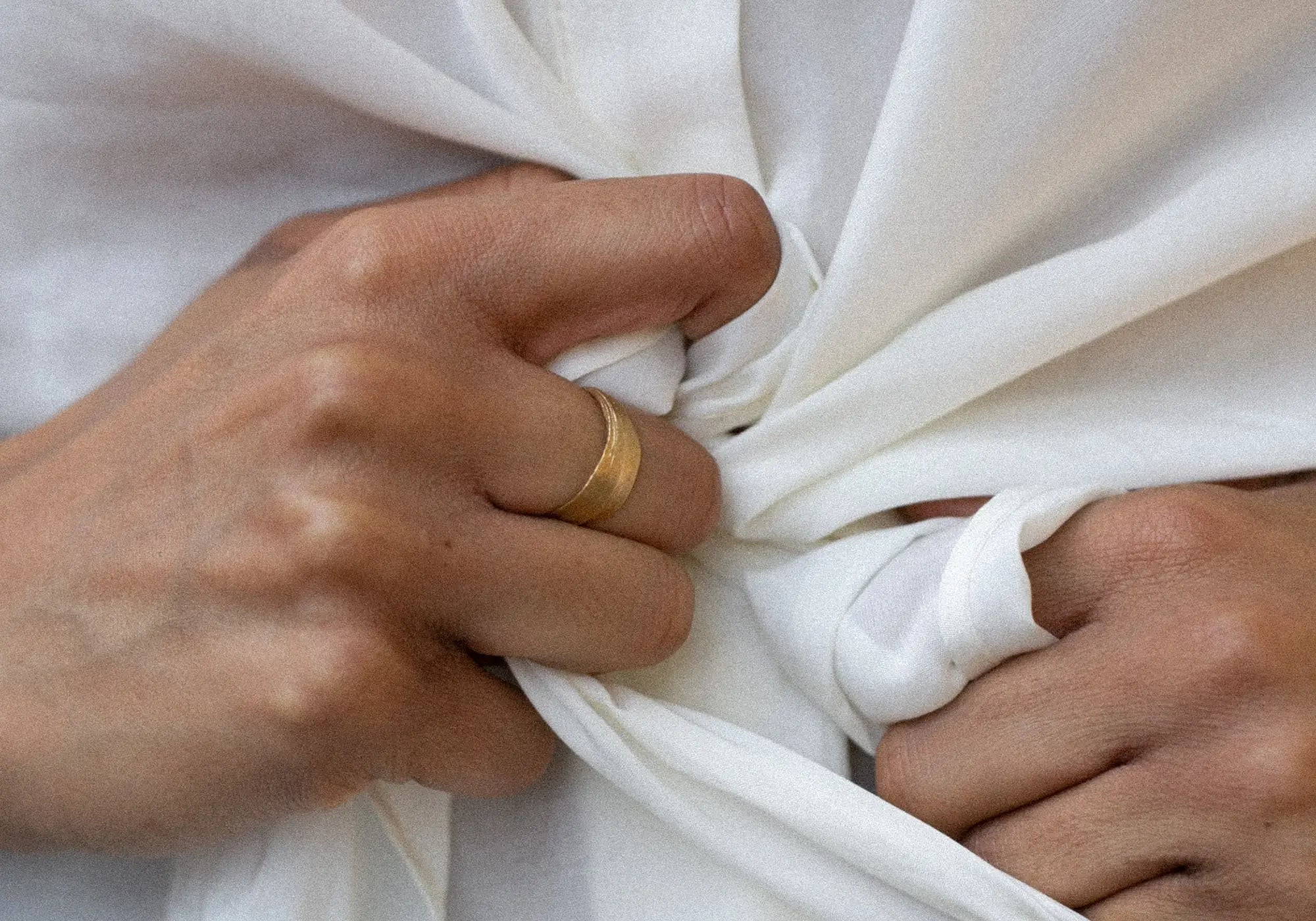 Close-up of hands holding white fabric with a gold ring on one finger.