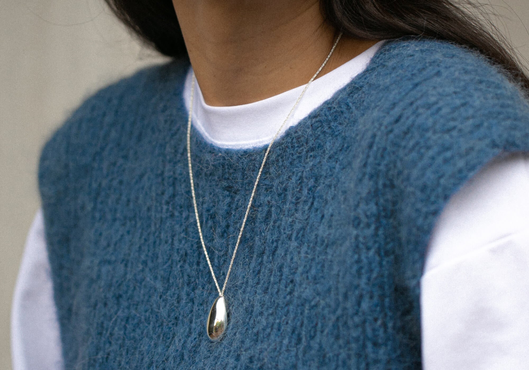 Person wearing a blue knitted vest over a white shirt with a necklace.