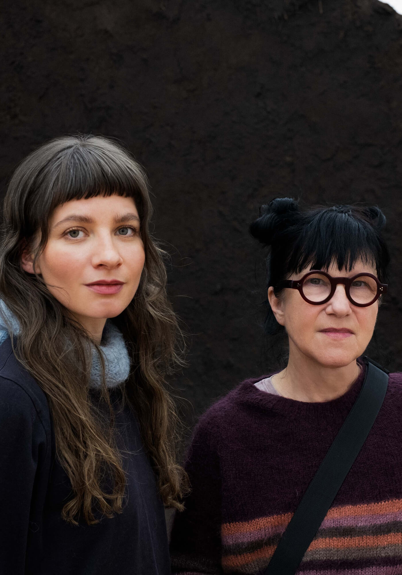 Two women standing side by side against a dark background